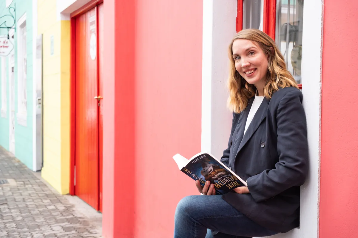Jana Marie Backhaus-Tors liest ein Buch vor einer korallroten Wand