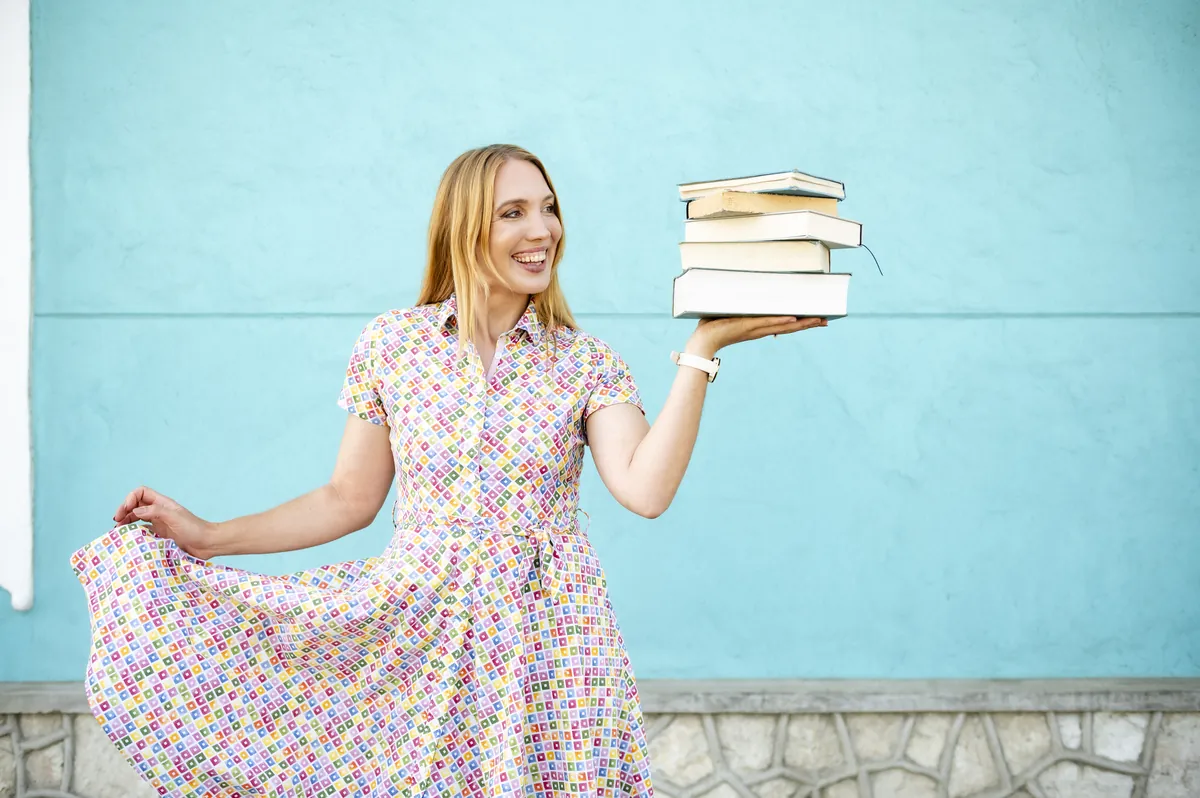 Jana Marie Backhaus-Tors mit einem Stapel Bücher vor einer hellblauen Wand