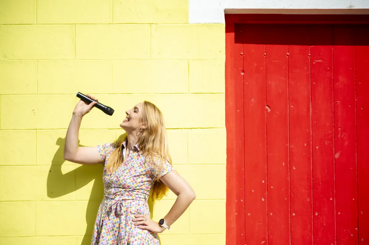 Jana Marie Backhaus-Tors singt in ein Mikrofon vor einer gelben Wand mit roter Tür