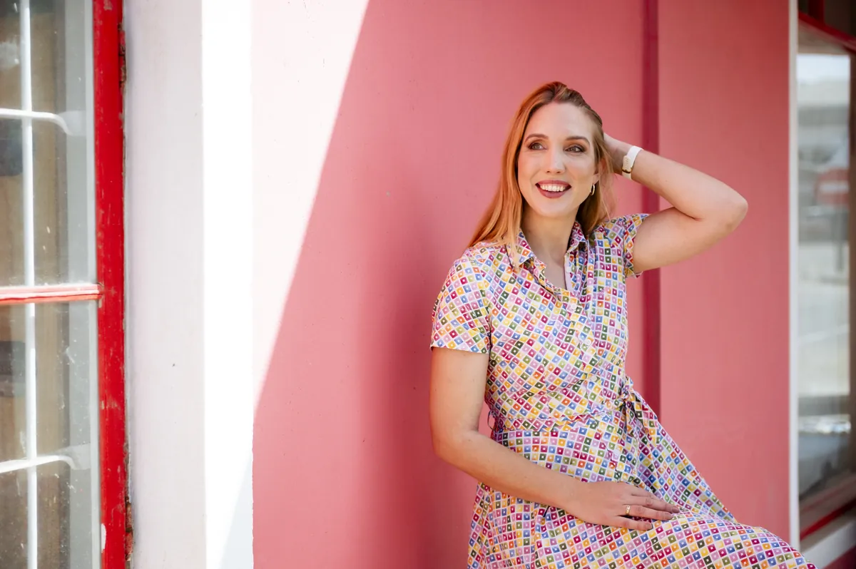 Jana Marie Backhaus-Tors sitzt lachend vor einer korallroten Wand